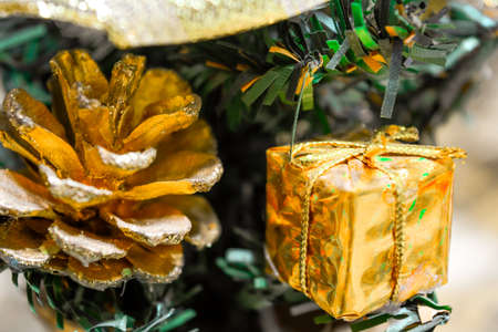 Closeup photo of little artificial green Christmas and New Year Fir-Tree with gold foil wrapped gift box, fir tree cone and gold ribbon bowの写真素材
