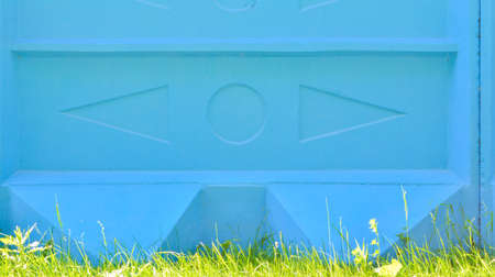 Outside cement block wall with convex embossed elements, under the wall grows green grass. Urban wall painted blue as backgroundの写真素材