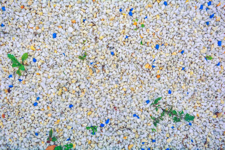Gravel texture of white, yellow, blue small natural stone rubble with sparse green grass plants. Natural crushed stone of rich color, young grass sprouted among stonesの写真素材