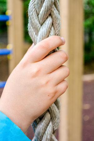 Close up of child hand clings to thick braided rope for climbing of children's sports equipment on...