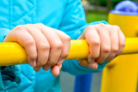 Close up of child hands holding metal bar of children's sports equipment on playground. Concept of...