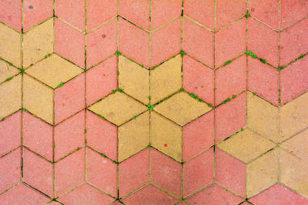 Red and yellow road tiles on city street pavement with growing grass in mortar. Road construction background. Cobblestone pathway paved with yellow and red rhombus bricks. Road cover surface textureの写真素材
