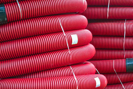Coils of new red plastic pipe with rain drops. Red plastic tubing for underground cable protection. First floor of a skein of red corrugated tube. Plastic pipes background. Detail of red tube coilの写真素材