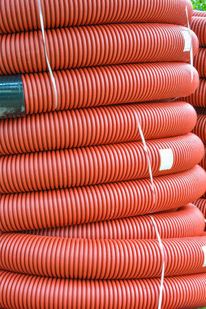 Coils of new red plastic pipe with rain drops. Red plastic tubing for underground cable protection. First floor of a skein of red corrugated tube. Plastic pipes background. Detail of red tube coilの写真素材