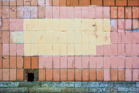 Brick wall of city house is made of vertical orange concrete tiles, some of which pink or yellow...