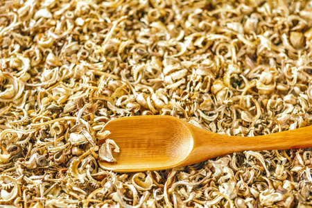 Wooden spoon on heap of scattered dry marigold seeds - healthy flowering plant for traditional...