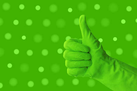 Hand in green protective rubber glove on green background with dots. Approved gloved hand thumbs up and showing ok. Concept of sanitation and hygieneの写真素材