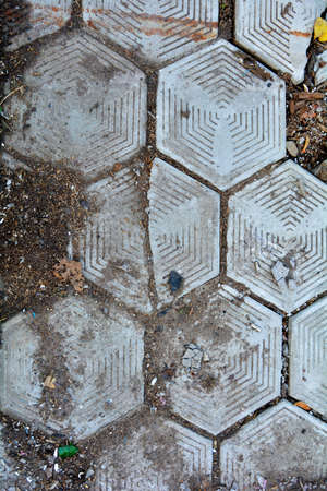Old damaged hexagonal stone block pavement for exterior with grass and fallen leavesの写真素材
