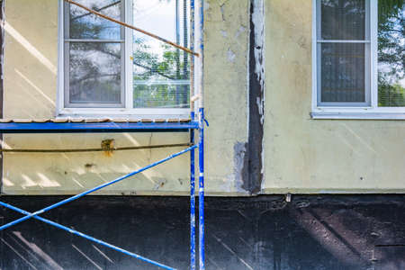 Outside repair and renovation of apartment house using blue paint metal scaffolding tower. Urban typical apartment building with scaffolding nearbyの写真素材
