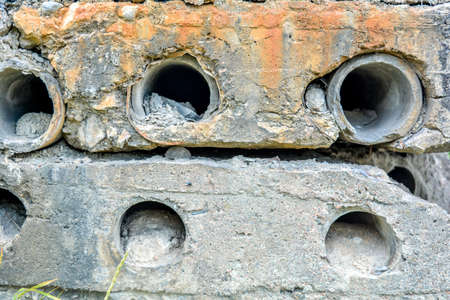 Side of old dilapidated concrete blocks with round through holes with drainage pipes. Close up of rough textured concrete wall with holes for pipeの写真素材