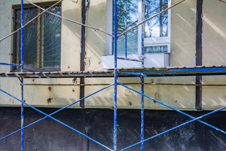 Outside repair and renovation of apartment house using blue paint metal scaffolding tower. Urban typical apartment building with scaffolding nearbyの写真素材