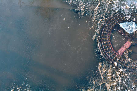 Puddle and closed sewer iron manhole with melted dirty snowの写真素材