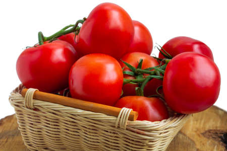 Fresh organic red tomatoes in a woven basket on cutting wood slice isolated on white. Close up photographyの写真素材