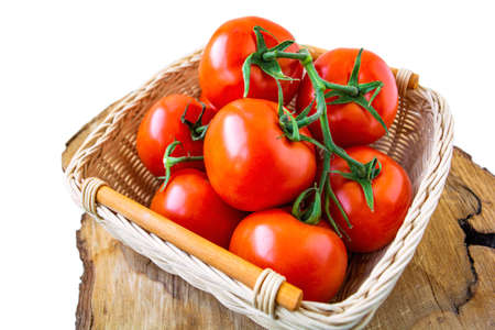 Fresh organic red tomatoes in a woven basket on cutting wood slice isolated on white. Close up photographyの写真素材