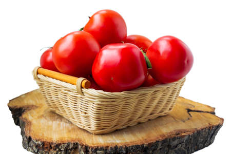 Fresh organic red tomatoes in a woven basket on cutting wood slice isolated on white. Close up photographyの写真素材