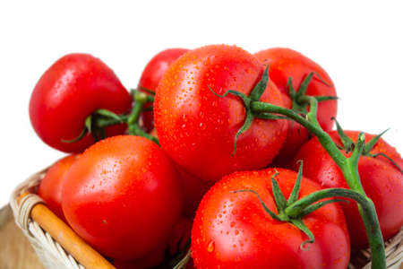 Fresh organic washed red tomatoes with water drops in a woven basket isolated on white. Close up photographyの写真素材