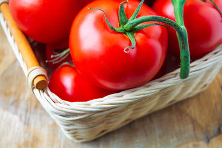 Fresh organic red tomatoes in a woven basket. Close up photographyの写真素材
