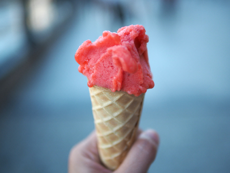 Woman's hands holding melting strawberry ice cream waffle cone in hands on blurred background.の写真素材