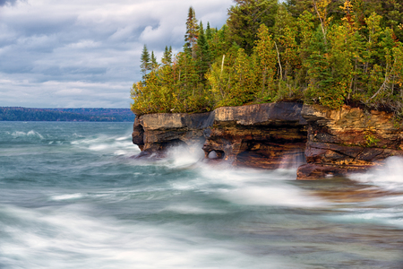 Crashing waves pound the rocky shoreline along Lake Superior near Munising Michigan. A slow shutter speed creates a silky and softer look of the stormy waters.の写真素材