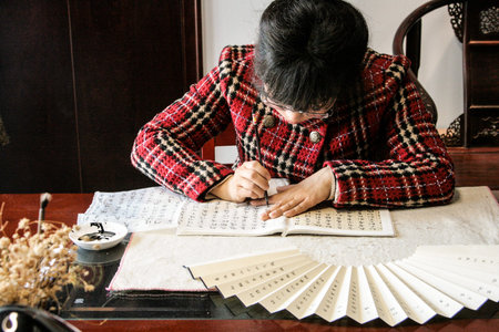 Hangzou, China - May. 22, 2016: Mrs Mai is writing down the chinese symbols on hand made fan