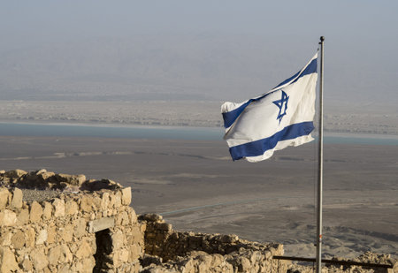 Israel flag on blue sky with ruin of Masada