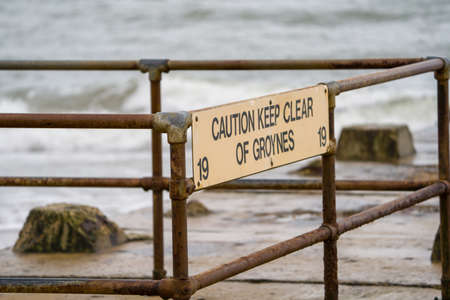 A sign on a fence at the beach with the inscription: Caution keep clear of groynesの写真素材