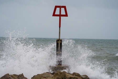 Stormy sea waves crashing on a breakwater with red warning sign.の写真素材