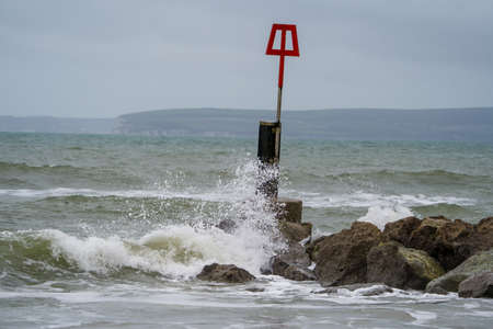 Beach breakwater with red warning sign in stormy weather.の写真素材