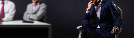 Businessman in suit sitting in armchair with his team in backgroundの写真素材