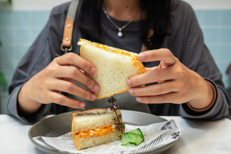 Closeup of a woman eating a sandwich with vegetables and cheese.の写真素材