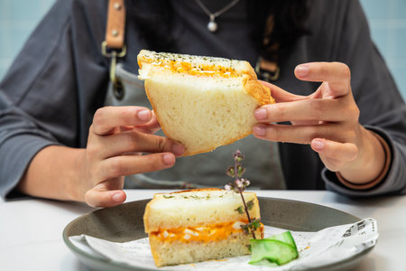 woman hands hold a sandwich with cheese and cucumber on a plateの写真素材
