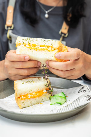 Close up of woman eating breakfast sandwich with egg and vegetables in cafeの写真素材