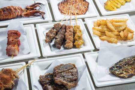 Skewers of grilled fish, squid and chips on white platesの写真素材