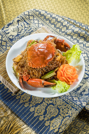 A whole crab served over glass noodles with lettuce, green onions, and carrot flower on a festive Thai plate.の写真素材