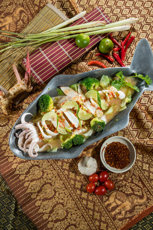 Sliced squid with lime and chili served in a fish-shaped plate with Thai herbs and vegetables.の写真素材