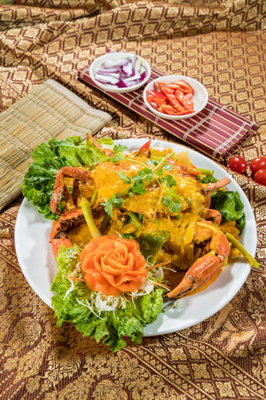 Thai crab curry dish with cilantro, cabbage, and carrot flower garnish, served on a white plate with traditional Thai fabric and bamboo mat.の写真素材