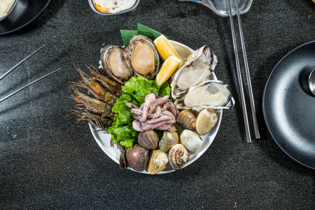 A plate of assorted raw seafood including oysters, clams, abalone, shrimp, and squid, garnished with lettuce and lemon.の写真素材