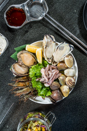 A white plate of assorted raw seafood including oysters, clams, abalone, shrimp, and squid, garnished with lettuce and lemon.の写真素材