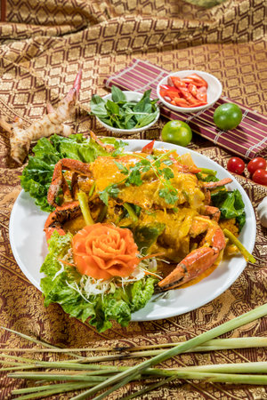 Thai-style crab in yellow curry sauce, garnished with cilantro and vegetables, served with lime, chili, and Thai herbs.の写真素材