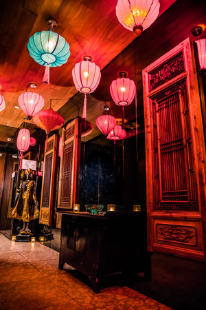 Ornate East Asian interior with red and turquoise lanterns, carved wood panels, and a statue centerpiece, evoking a warm and immersive ambiance.の写真素材
