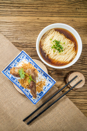 A bowl of noodle soup with dark broth and green onions, served with braised meat on garlic bits and cilantro. Rustic table enhances tradition.の写真素材