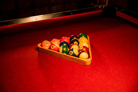 A triangle rack of colorful billiard balls arranged on a red pool table, ready for a game.