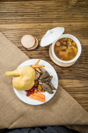 A traditional Chinese herbal chicken soup with medicinal ingredients, served in a ceramic bowl and rustic setting.の写真素材