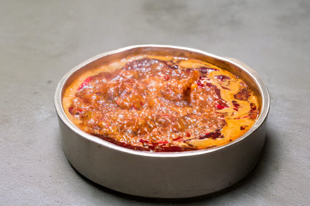 A pot of spicy Chinese hot pot soup base boiling on an induction stove. Red chili oil and steam...