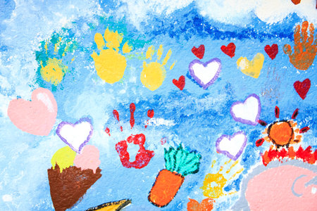 A vibrant mural with colorful handprints, hearts, sun, carrot, and ice cream cone on sky-like background.の写真素材