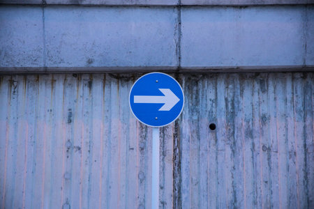 A blue circular traffic sign with a white arrow mounted on a pole in front of a ridged concrete...