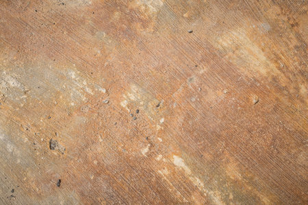 A close-up of a weathered concrete surface with earthy tones and embedded debris, showing rough...
