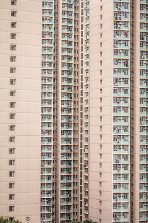 A beige high rise building with grid like facade, vertical and horizontal lines, air conditioners, and laundry, reflecting urban density.の写真素材