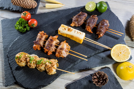 Five gourmet skewers with grilled meat, tofu, seafood, and vegetables, served with fresh garnish and decorative elements on slate boards.の写真素材