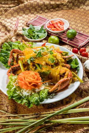 Thai-style crab coated in yellow curry sauce, garnished with cilantro, lettuce, and carved vegetables, surrounded by fresh Thai ingredients.の写真素材